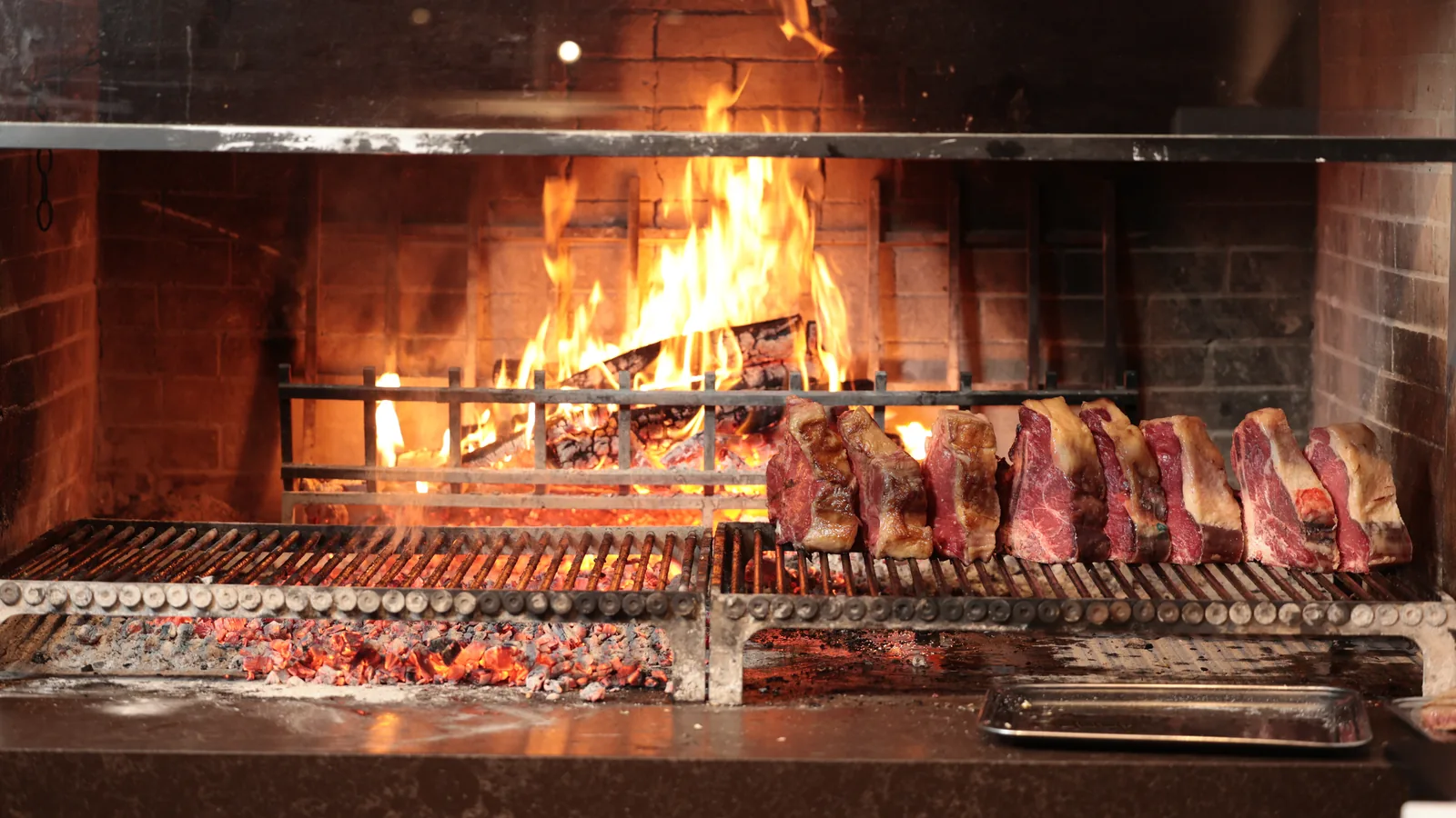 Costate frollate sulla griglia del caminetto, con le fiamme della legna di faggio e quercia